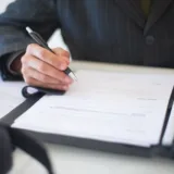 O persoană completează documente oficiale pe un birou de lucru