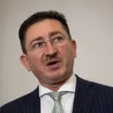 Bogdan Chiritoiu speaking to the press with multiple microphones and logos in the background