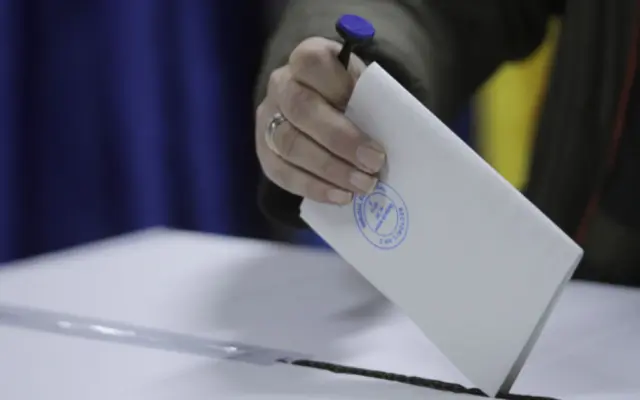 O mână introduce un buletin de vot într-o urnă