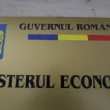 O placa aurie montata pe un perete, reprezentand firma oficiala a Ministerului Economiei din Romania, continand stema tarii, tricolorul si denumirea institutiei