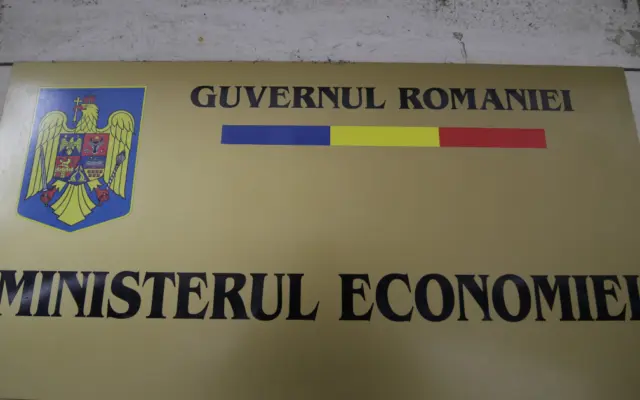 O placa aurie montata pe un perete, reprezentand firma oficiala a Ministerului Economiei din Romania, continand stema tarii, tricolorul si denumirea institutiei