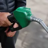 A person holding a green fuel nozzle at a gas station, symbolizing diesel fuel consumption