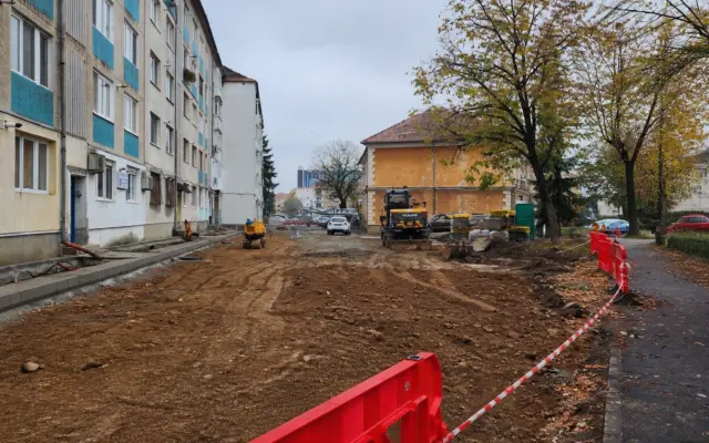 A construction site for a parking lot between residential buildings with excavators and red safety barriers