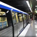 Un tren de metrou model CAF oprit în stația de metrou Piața Romană din București, cu câțiva călători pe peron și luminile stației aprinse