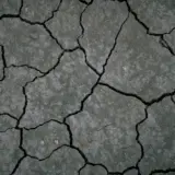 O vedere de sus a unui sol foarte uscat, crăpat în profunzime, cu o textură pământie, gri-maronie, fără vegetație vizibilă, ilustrând eroziunea și seceta