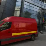 A red Poșta Română delivery van parked in front of a modern glass office building headquarters