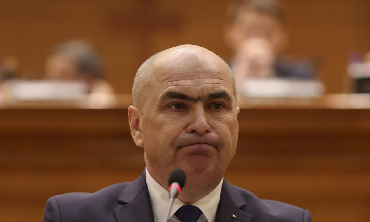 Bărbat la costum susținând o declarație oficială în fața unui microfon
