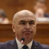 Bărbat la costum susținând o declarație oficială în fața unui microfon