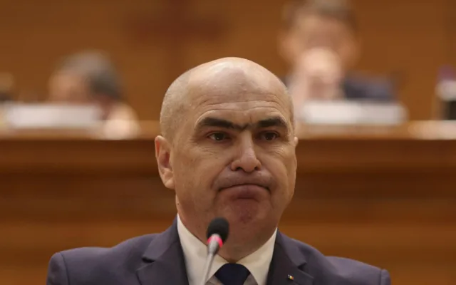 Bărbat la costum susținând o declarație oficială în fața unui microfon