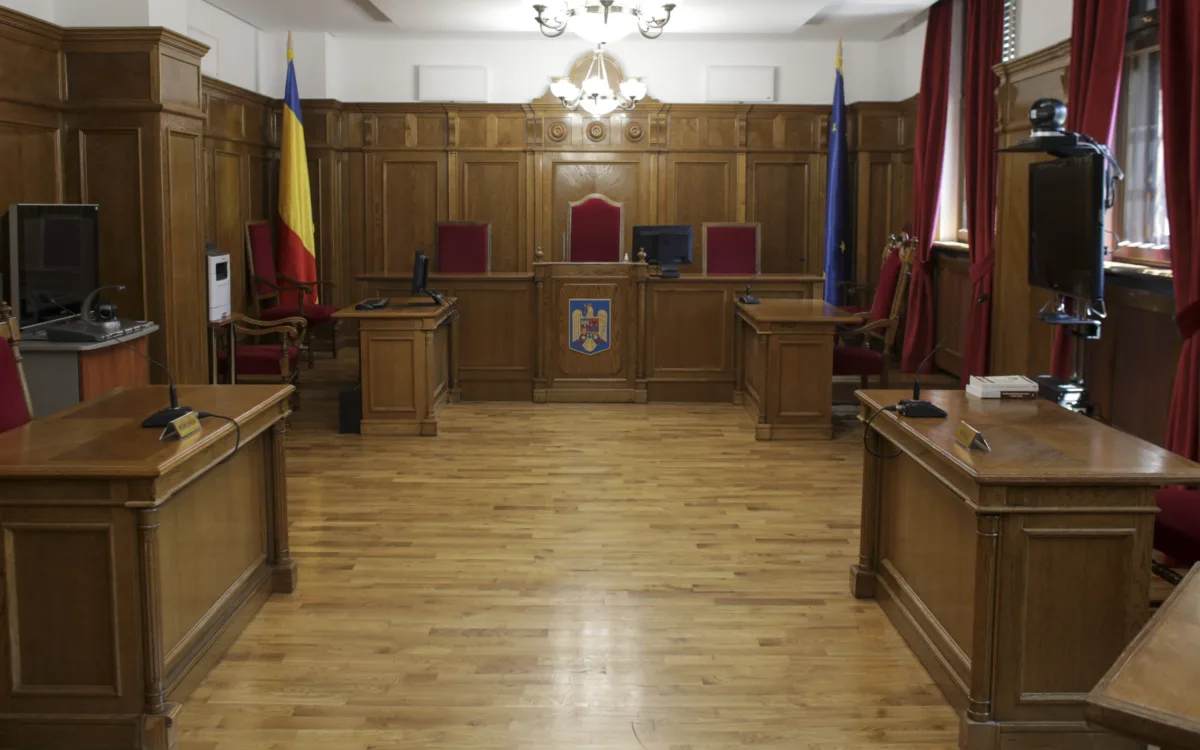 Interiorul unei săli de judecată cu steagul României în fundal