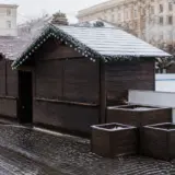 O serie de căsuțe de lemn închise, de tipul celor folosite la târgurile de Crăciun sau sezoniere, așezate pe un pavaj umed